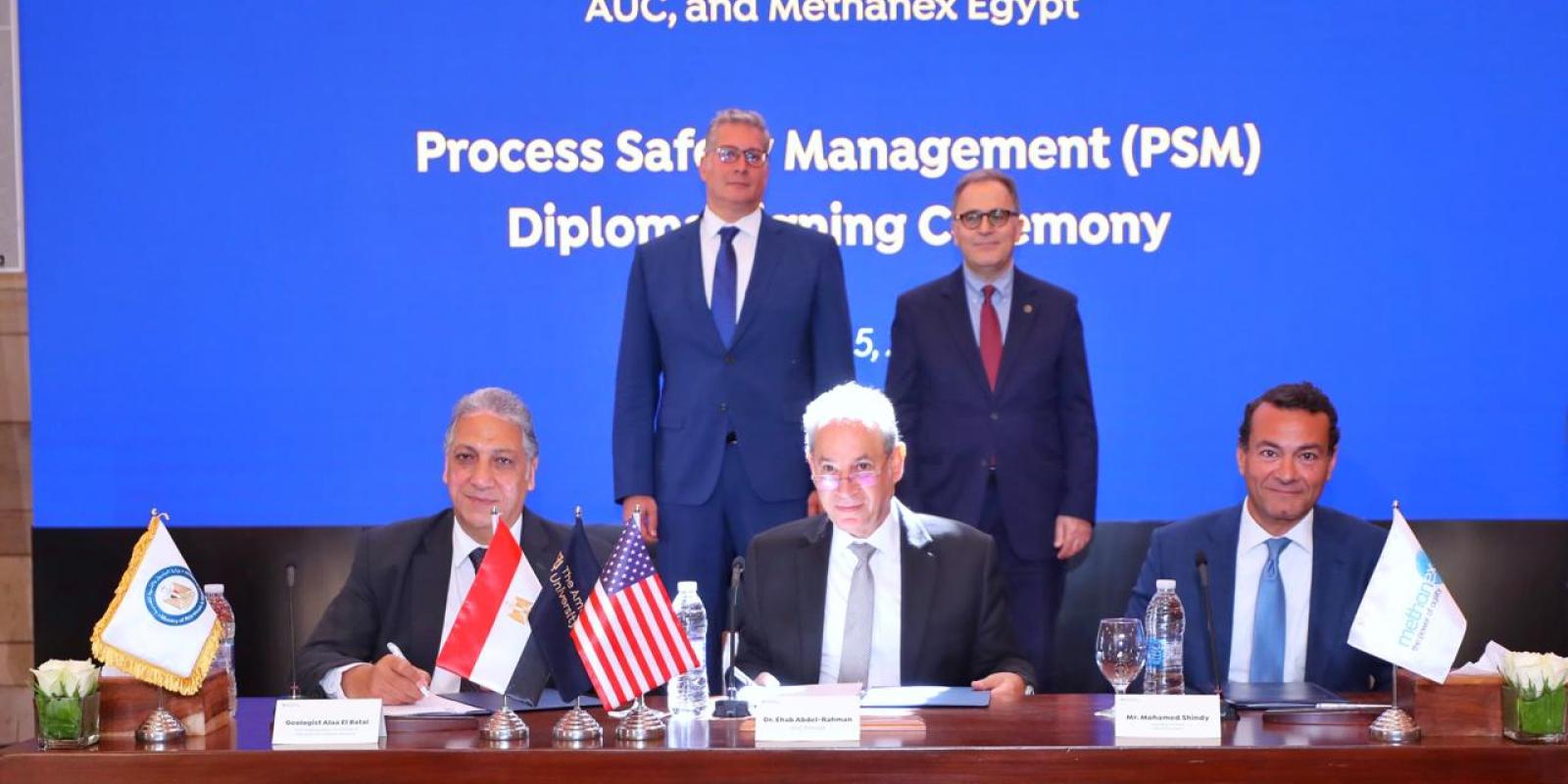 Senior officials from AUC, including the president and provost, sit and stand at a table to sign a memorandum of understanding.