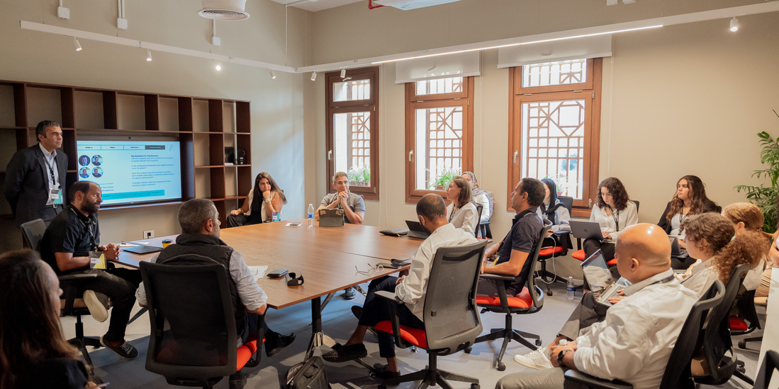a group of men and women sitting in a meeting room listening to a presentation