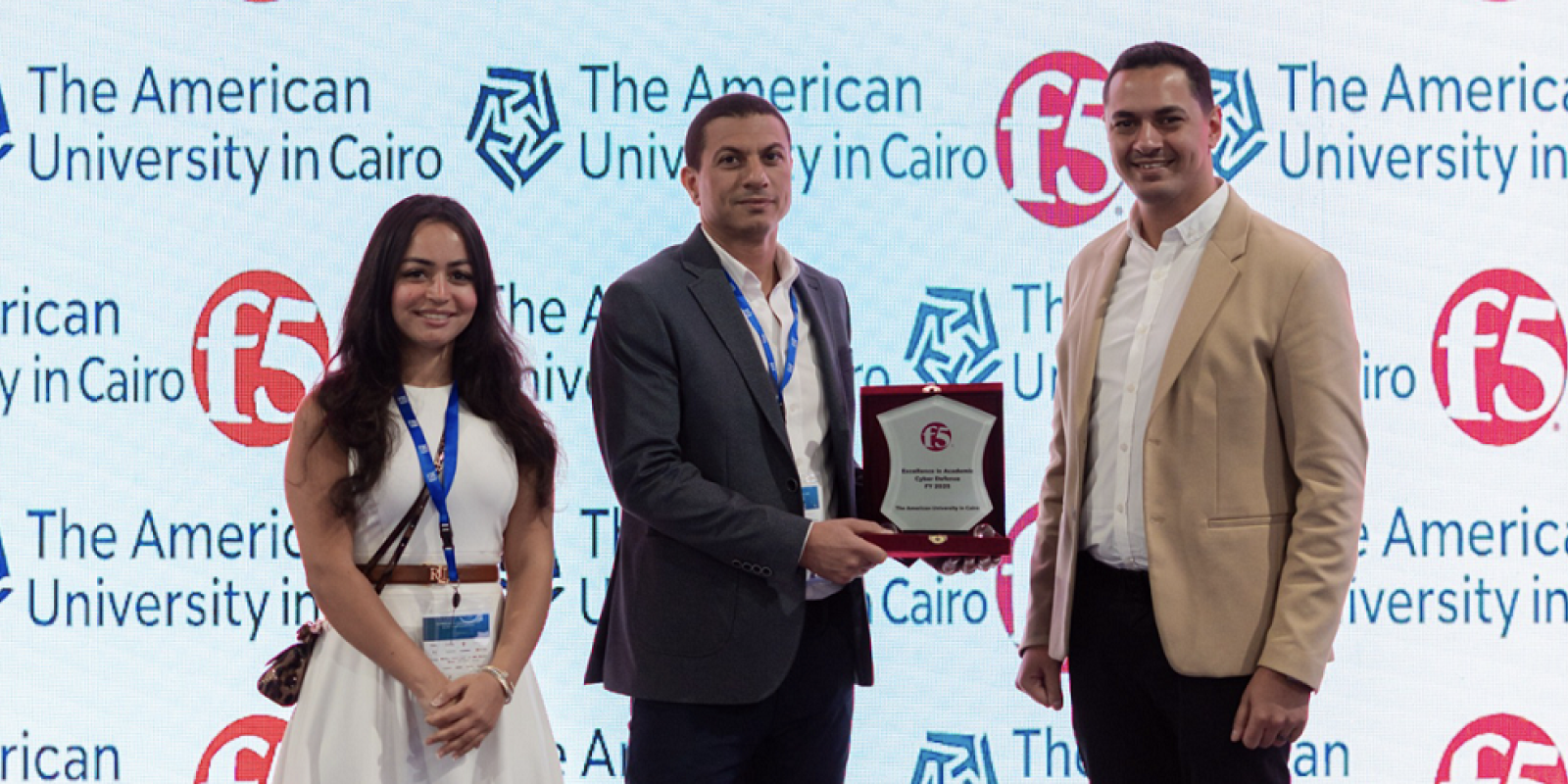 a lady wearing a white dress with two men wearing suits receiving an award