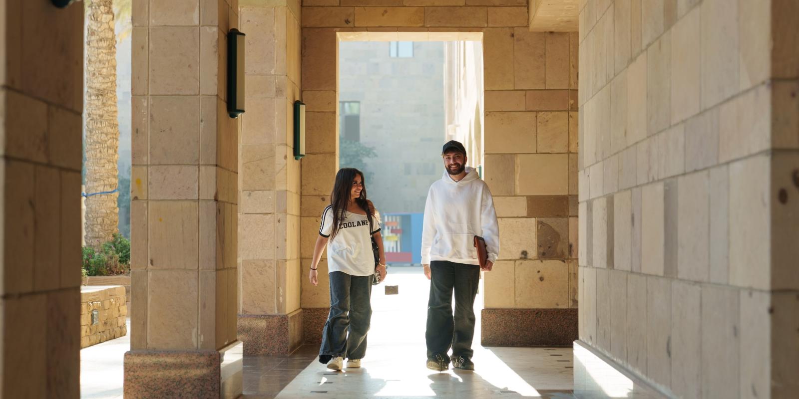 a girl and boy wearing white tshirts and blue jeans walking on campus