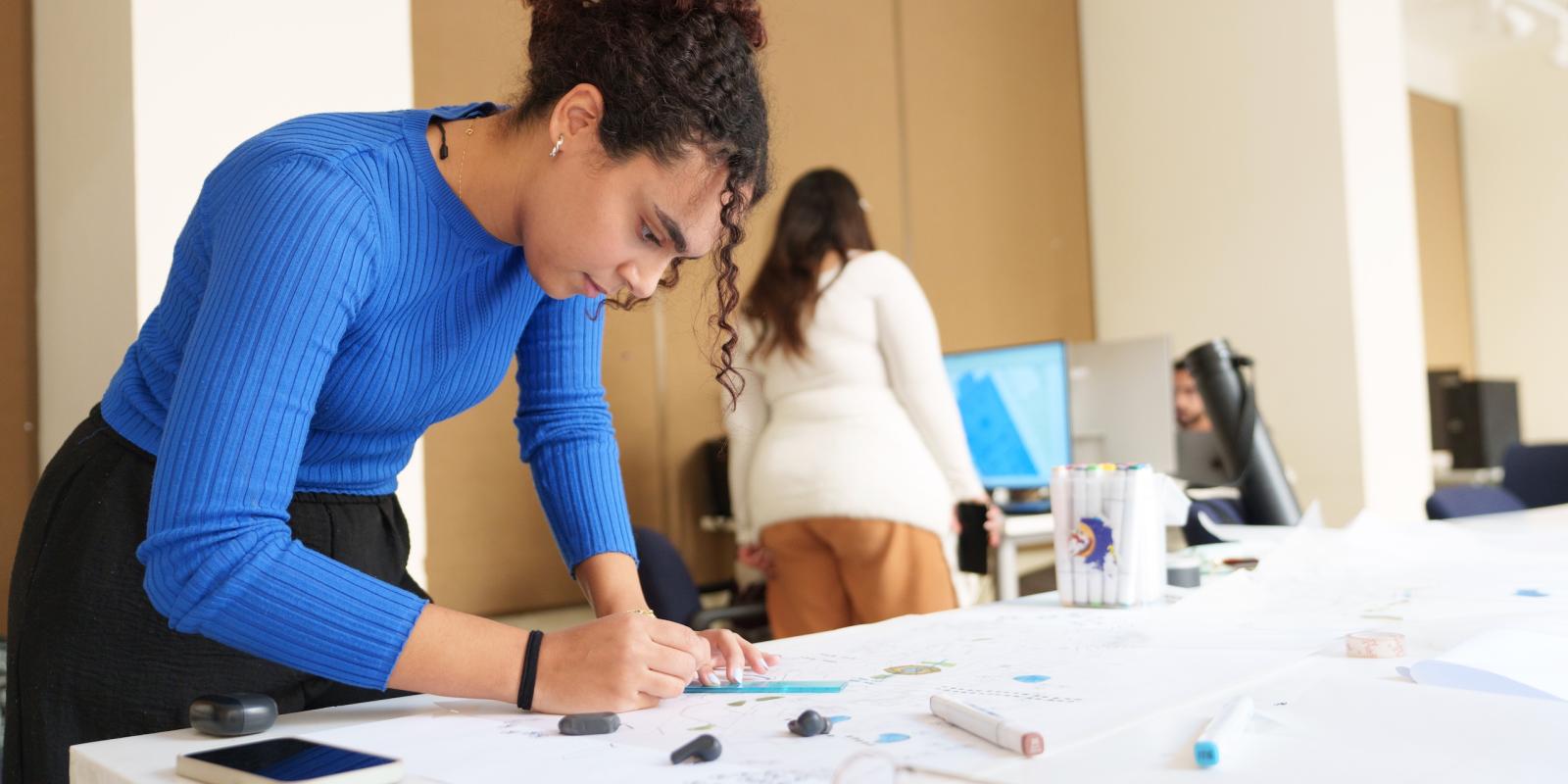 a girl with a hair bun wearing a blue shirt and drawing on a paper