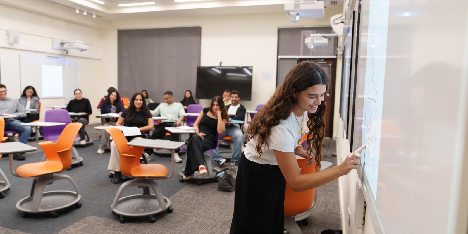 a girl in a classroom writing on the white smart board