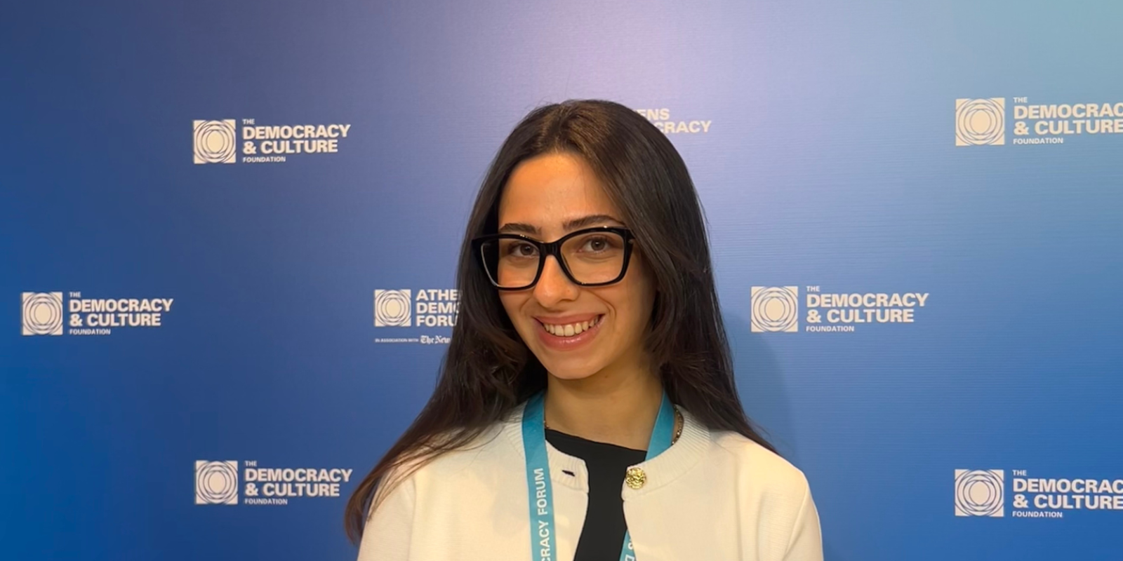 A picture of Laila Khalifa standing in front of a backdrop from the Athens Democracy Forum