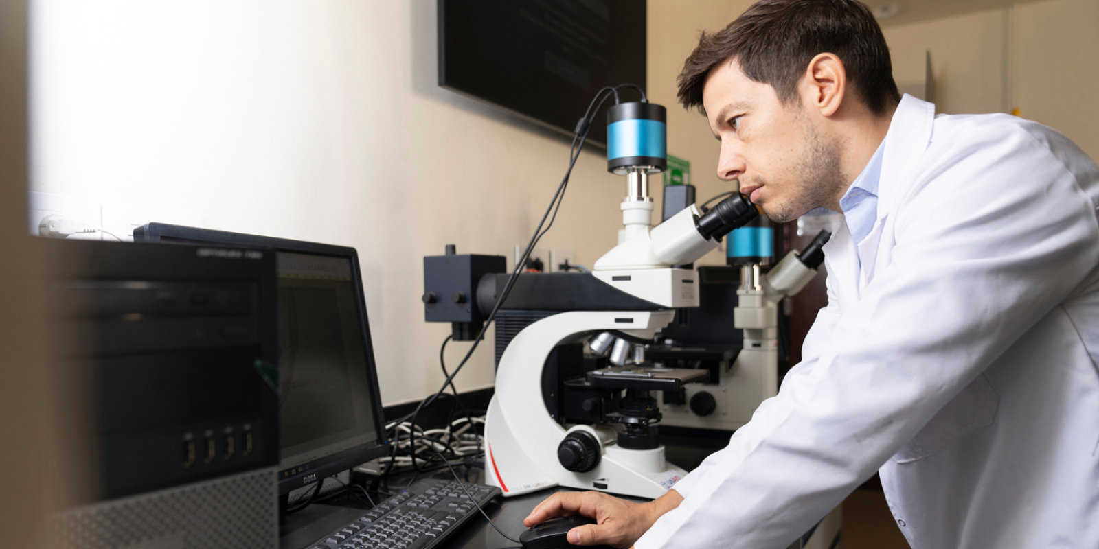 A scientist in a lab coat peers through a microscope.