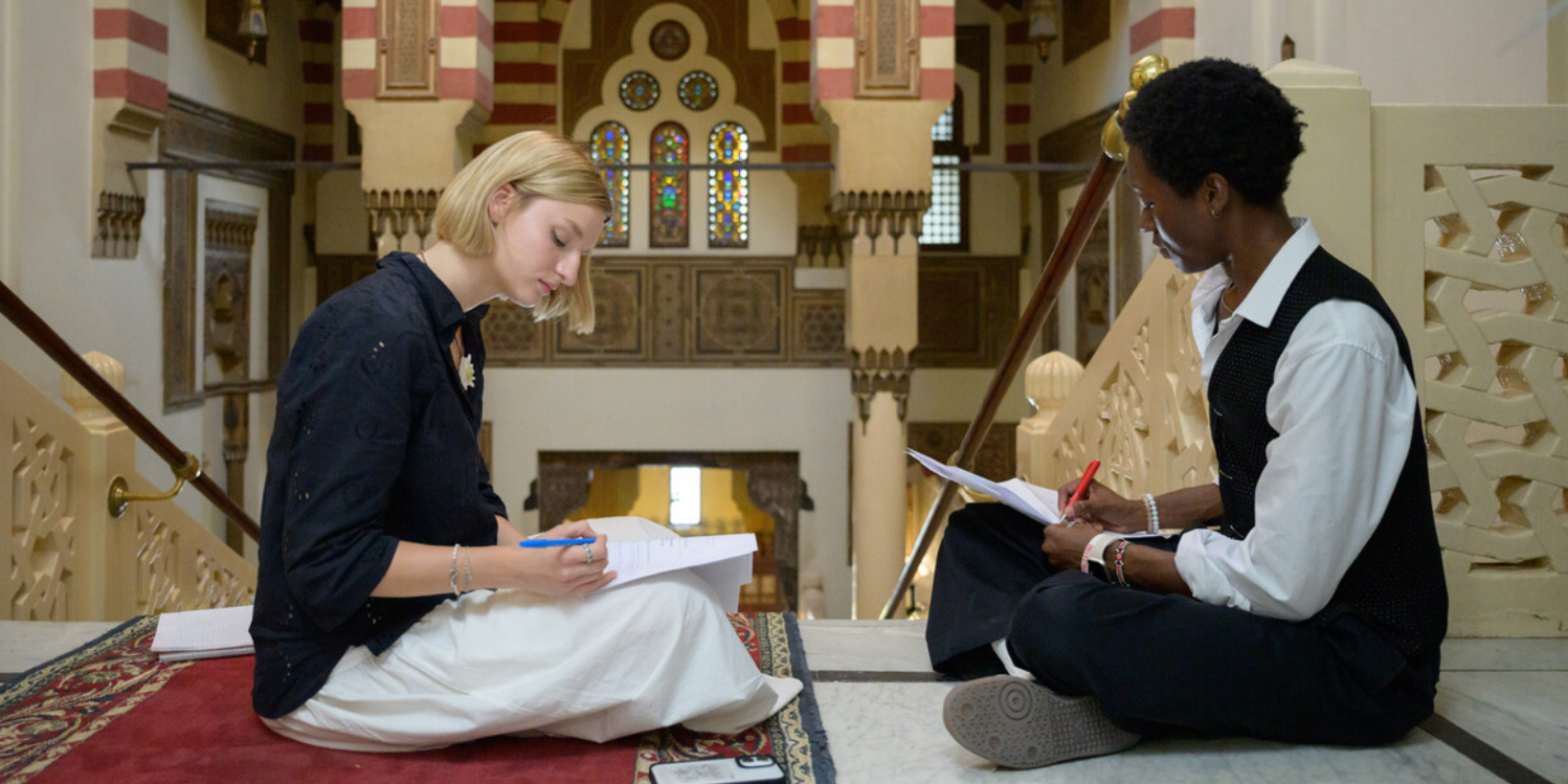 Two students sit and write at the top of a staircase
