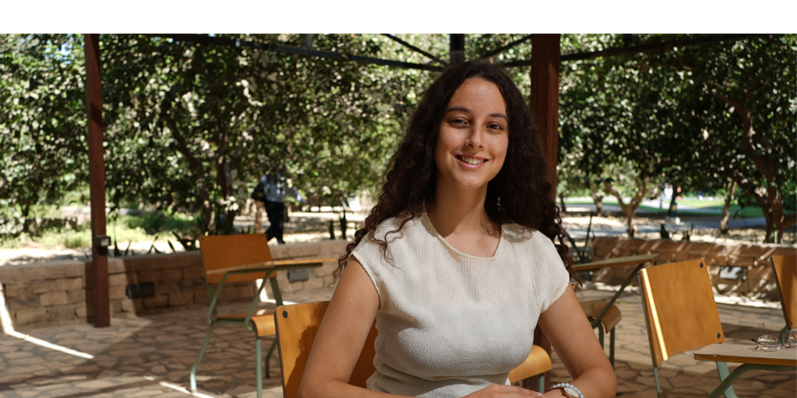 A student sits in a chair in an outside classroom surrounded by greenery.