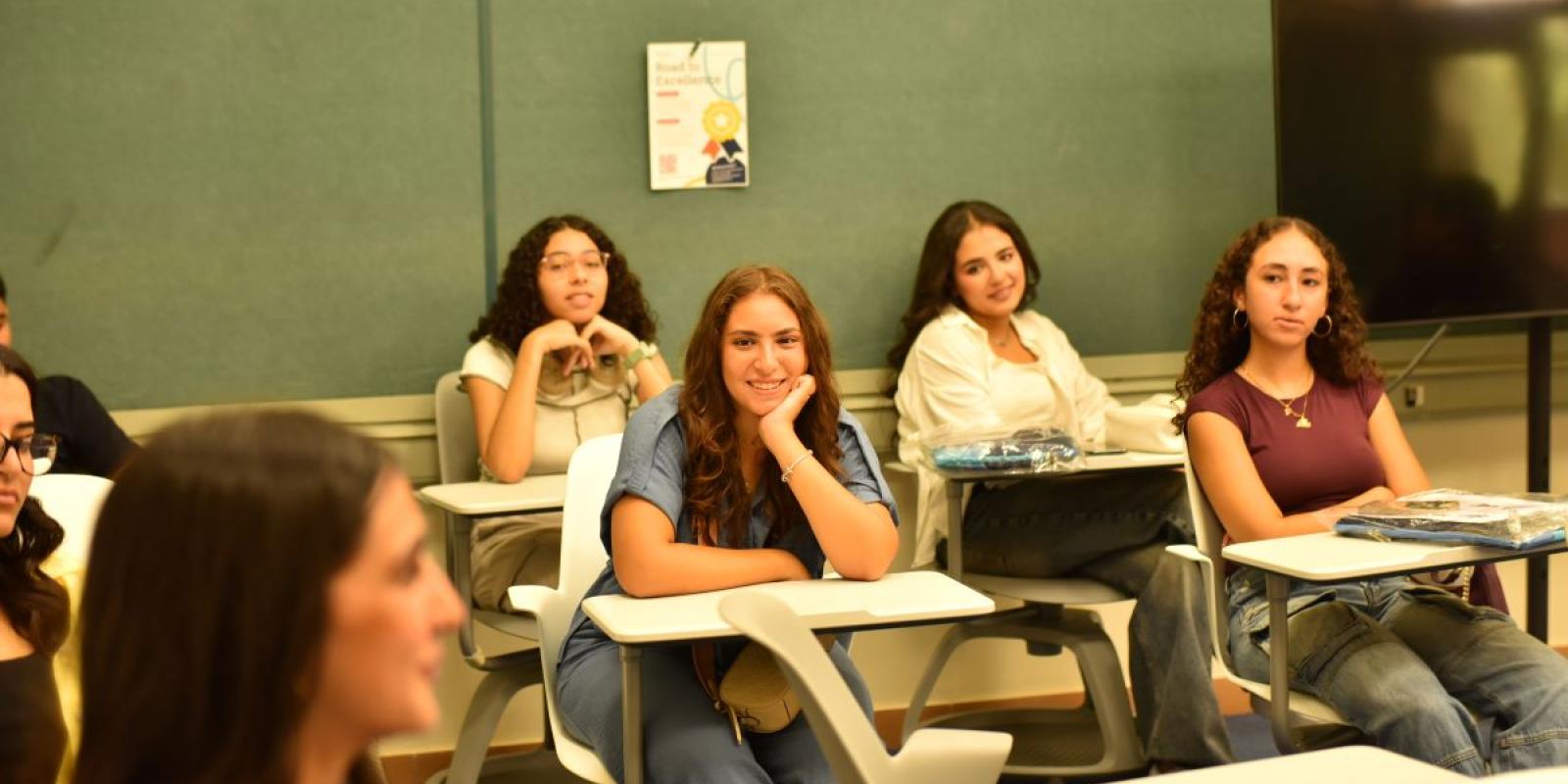 A bunch of students in a classroom listening to another student talk and they look interested.