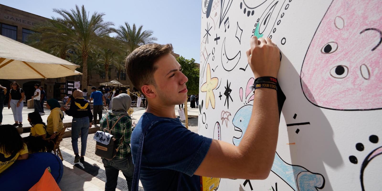 a boy wearing a black tshirt drawing on a white poster