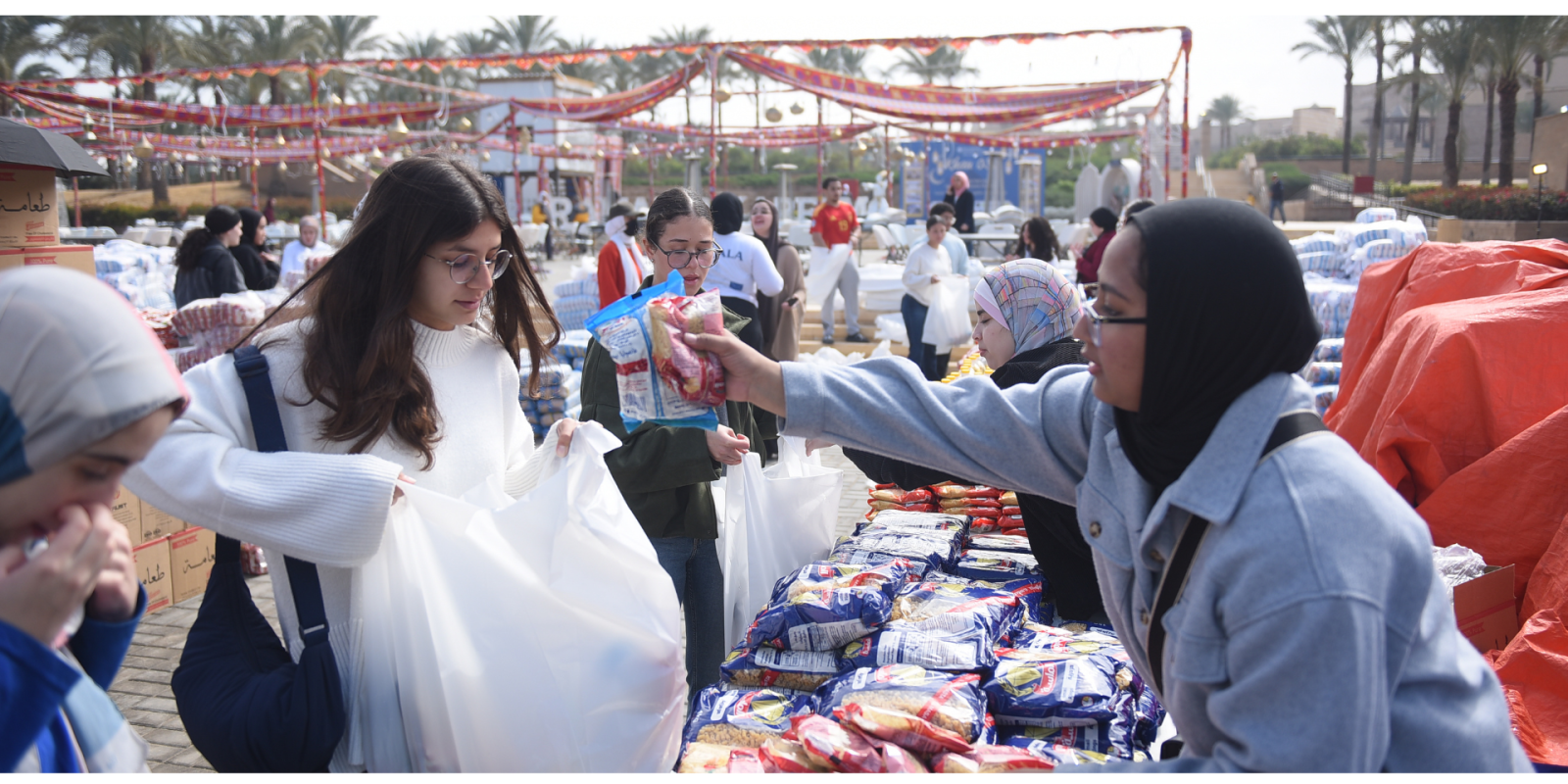 A young woman places bagged goods into a plastic bag of another young woman.