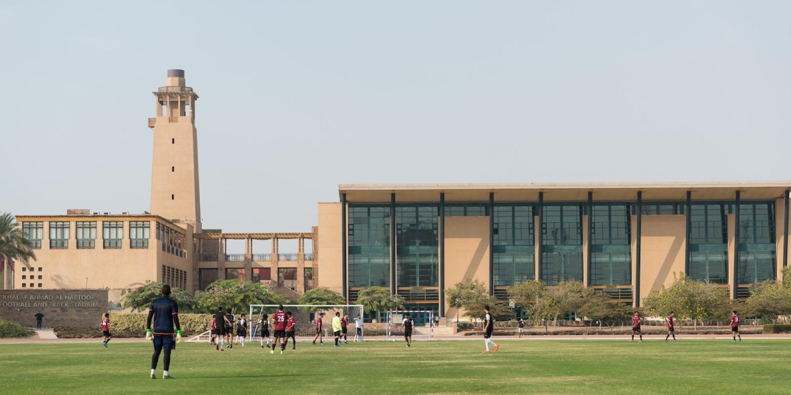 Students playing soccer on a grass field near AUC&rsquo;s Khalaf Ahmad Al Habtoor Football and Track Stadium.