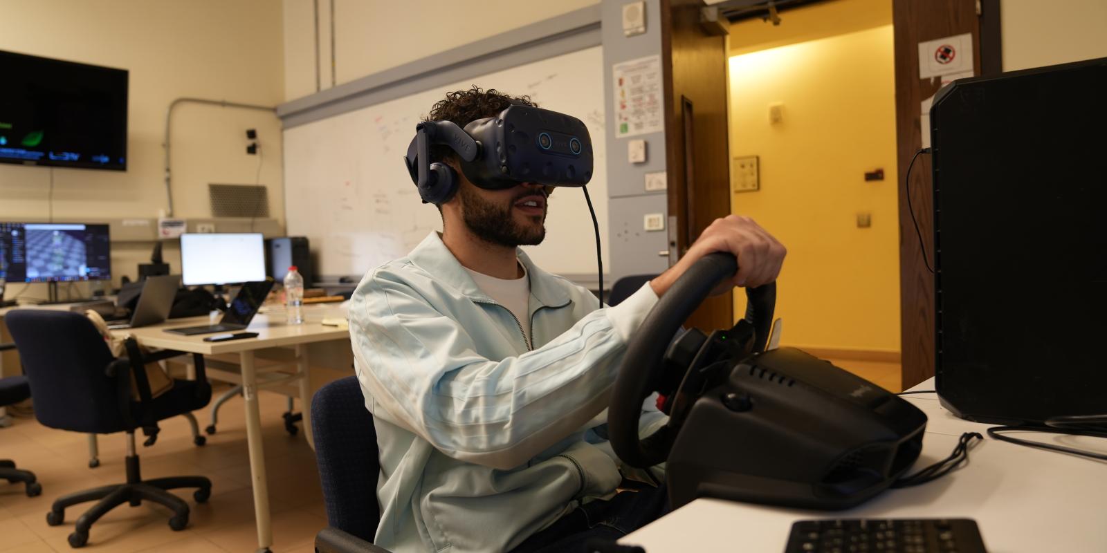 A person moves a steering wheel in a lab while wearing a vr headset