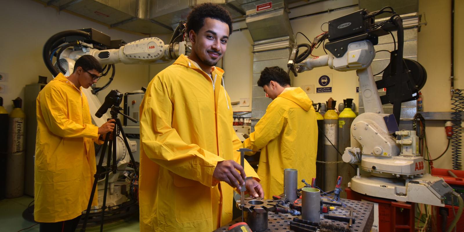 students wearing orange coats and working with machinary in engineering lab