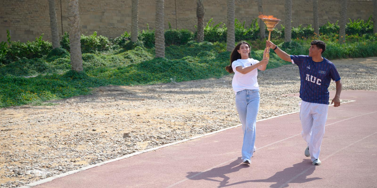 Two students holding the torch while running on track