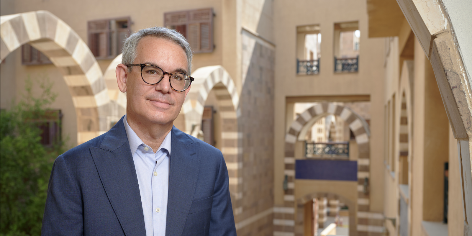a man wearing a suit and glasses, standing in the architecturally hollow space inside the HUSS building