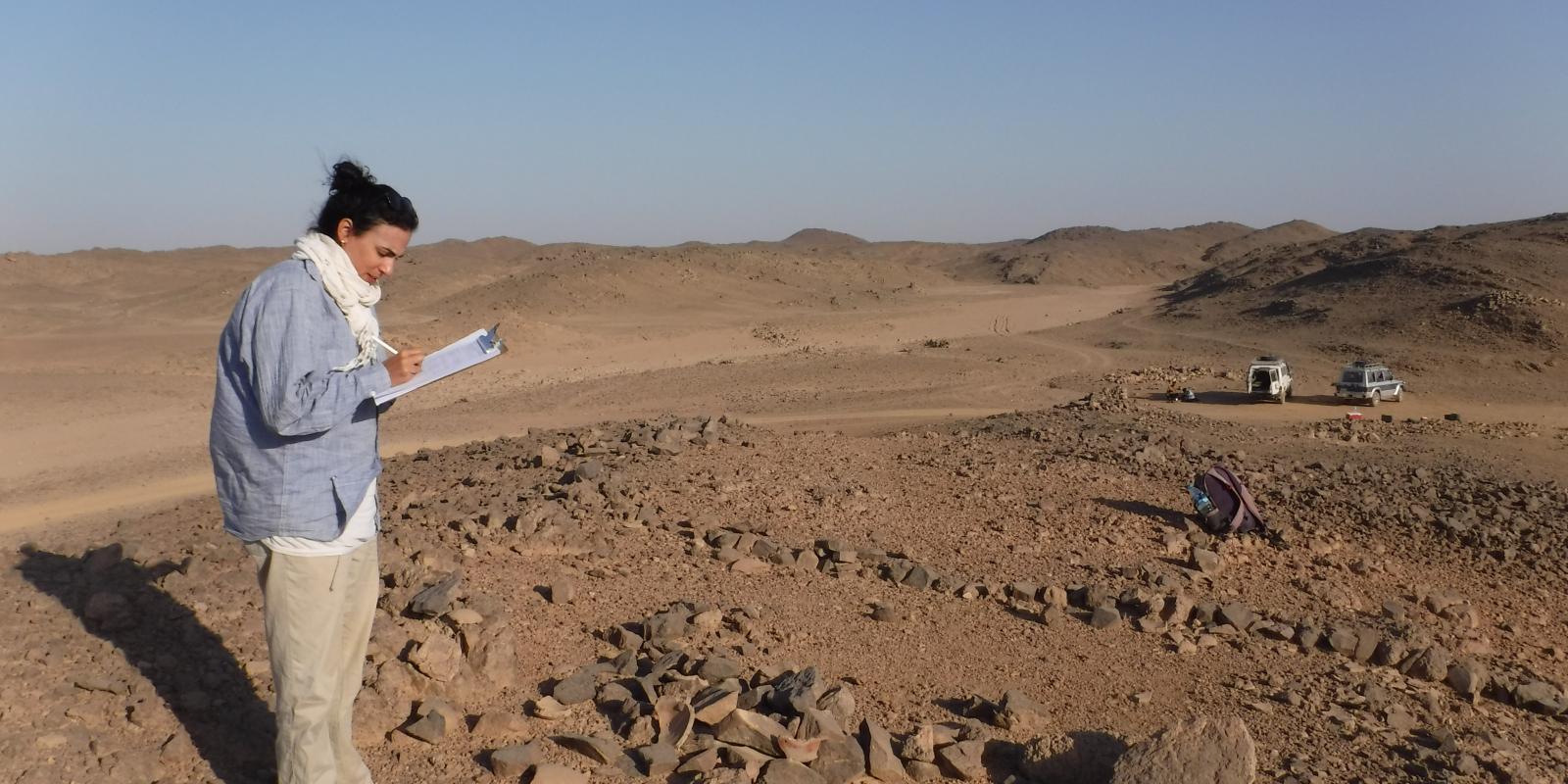 Meredith Brand standing in desert ruins holding a clipboard