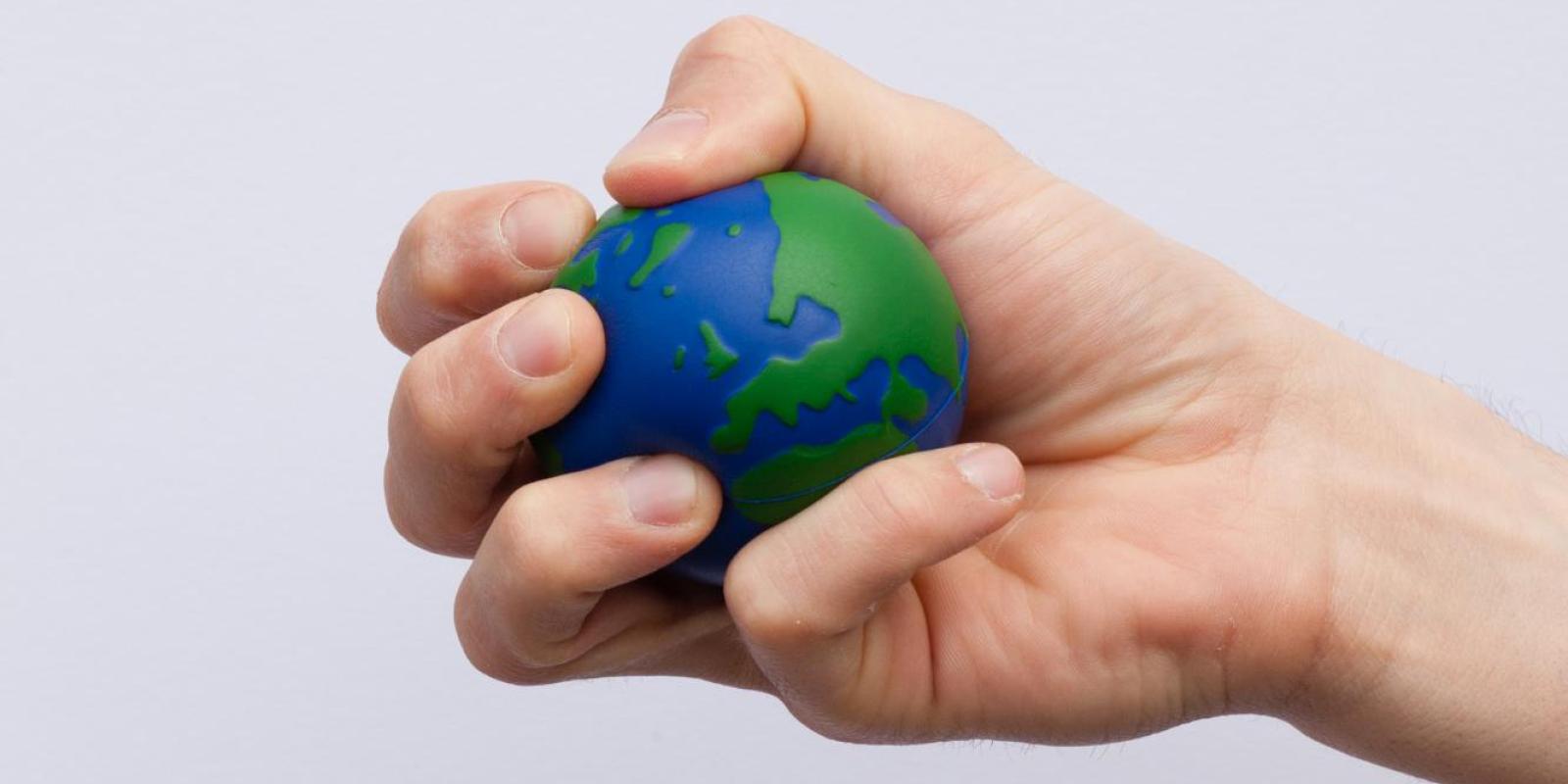 a hand catching an earth globe stress ball, the globe refers to the climate change challenges 