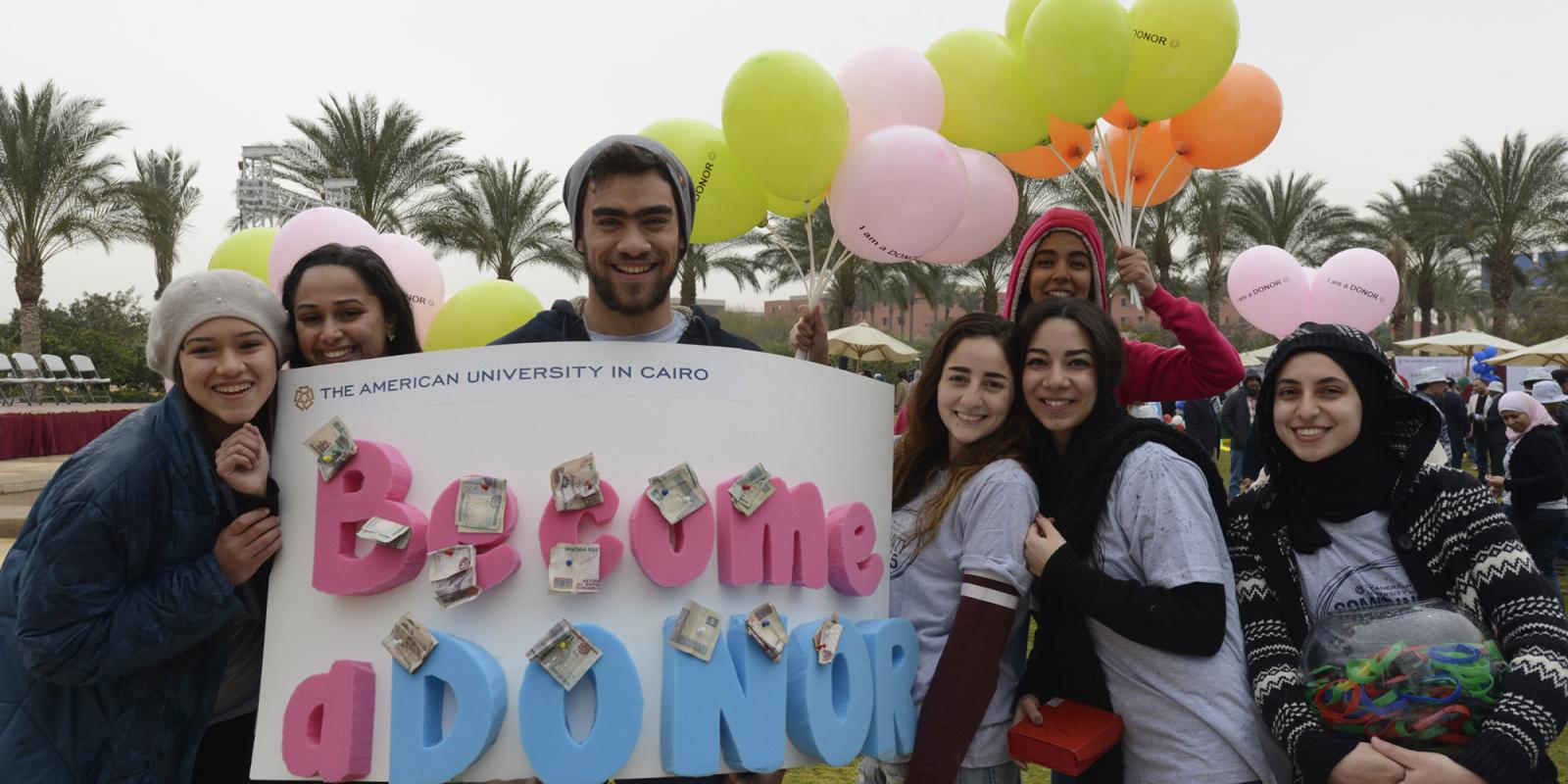 AUC community members holding banner saying "Become a donor"