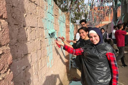 AUC student volunteers paint walls near a home in Fayoum