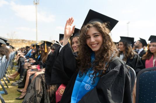 Students in cap in gown sit at commencement