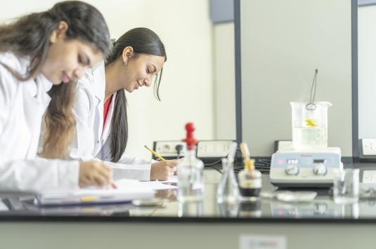 Two young women work on a counter in a science lab with glass beakers in front of them