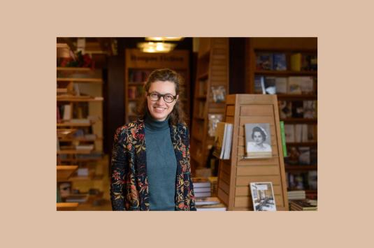 Photo of Veerle De Laet standing and smiling next to book shelves