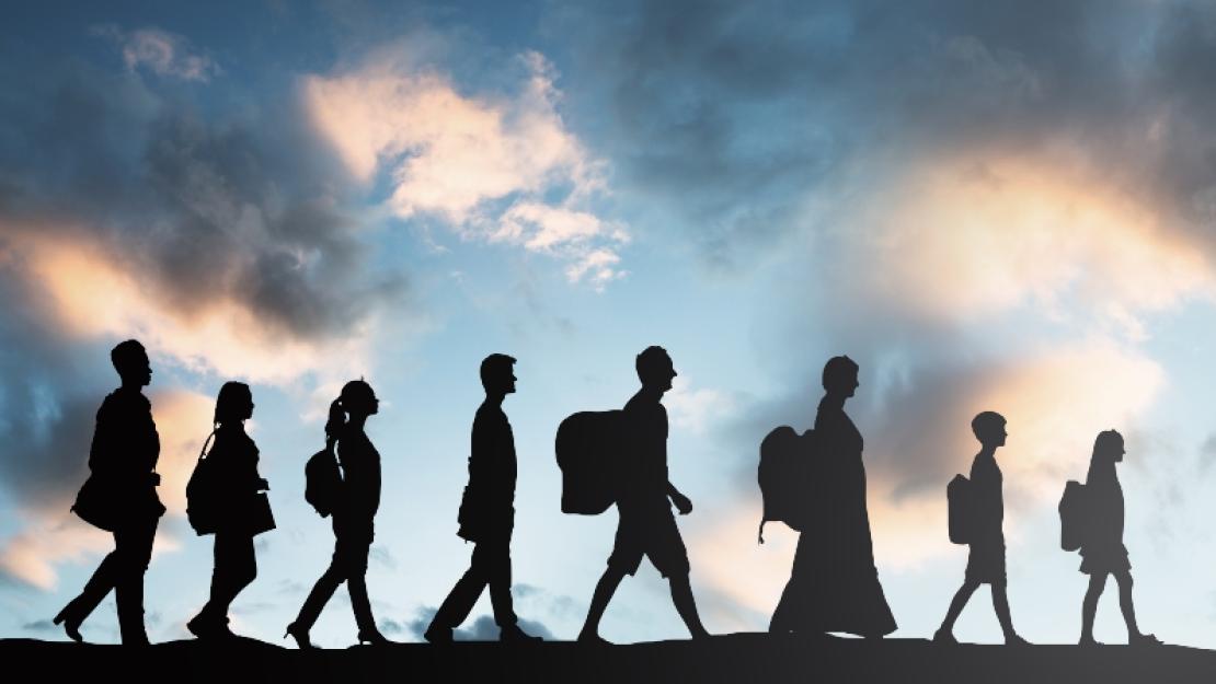Silhouette of people walking in a line with the sky illuminated behind them