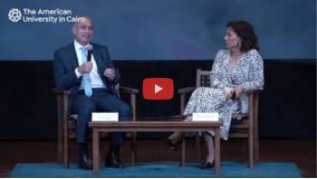 A woman and a man sitting down, the man is talking into a microphone