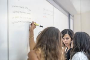 Three girls writing on a whiteboard in a classroom