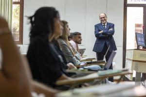 Students in class with a professor standing with hands crossed smiling at the students