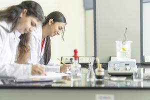 Two girls wearing a white lab coat writing in their notebooks in a lab