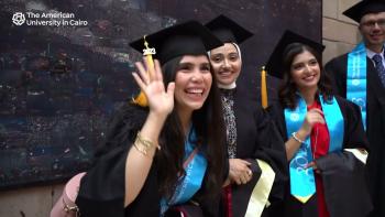 Three females are sitting and a male is standing and wearing their caps and gowns