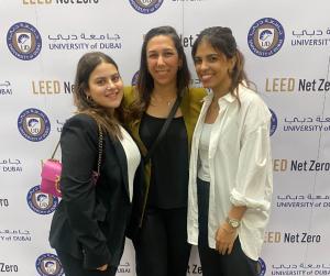 three women stand smiling in front of a vinyl backdrop containing the COP28 logo