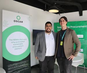 Two men stand smiling in front of a presentation booth