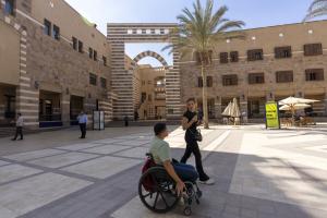 A boy sitting on a wheelchair and a girl is walking beside him