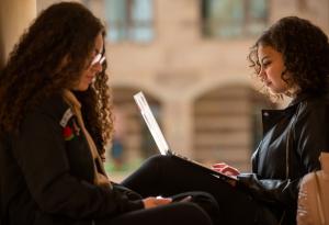 Two girls sitting together with one girl holding a laptop