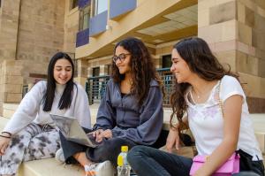 A group of three students sitting together smiling and looking a laptop