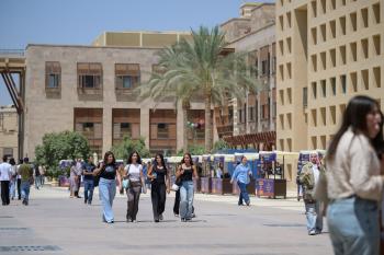 Males and females are walking in an open space. There are buildings around them
