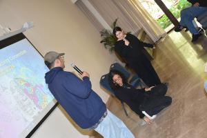 A male and a female are talking into a microphone to a female who is sitting on the floor