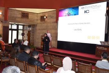 A woman is talking into a microphone in front of an audience. Text: Unlocking the Power of Global Education. Laila ElSerty