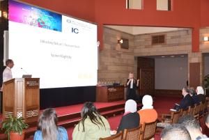 A woman is talking into a microphone in front of an audience. There is a big display screen behind her. Text: Unlocking Nature's Treasure Chest. Yasmin Maghraby