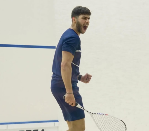 A male is holding a squash racket and shouting