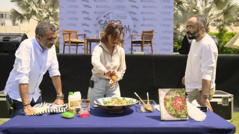 Yasmine (author) pours date molasses into a bowl of Freekeh with the photographer and moderator standing by in front of the stage at AUC Tahrir outdoors.