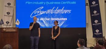 Co-founders of the Silver Screen Film School, a man and a woman, standing on stage speaking to the audience against a backdrop that says, "Congratulations to all our graduates"