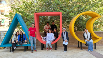 A group of students and professor poses outside the AUC logo