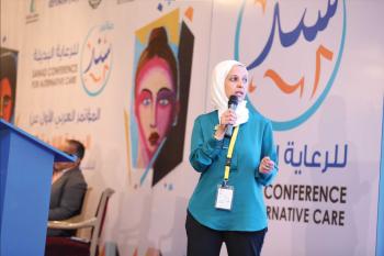 Yasmine El Hagry speaks at a podium holding a microphone and standing.