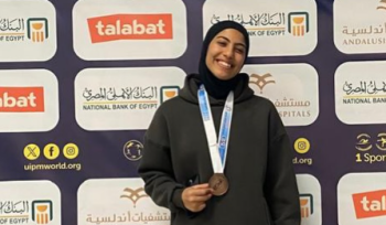 A female athlete is standing and smiling. She is holding a medal