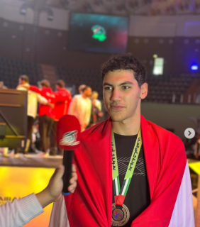 A male athlete is smiling. He is wearing a bronze medal and the Egyptian flag on his shoulders