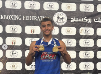 A male athlete is smiling. He is holding two gold medals. Text: Kickboxing Federation
