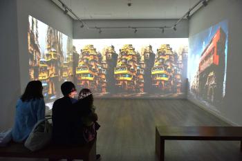 Two people and a child watch a wall projection in a art gallery
