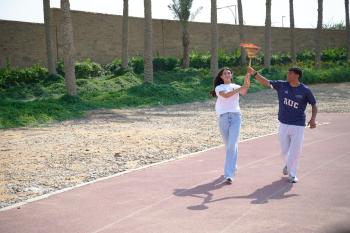 Two students holding the torch while running on track